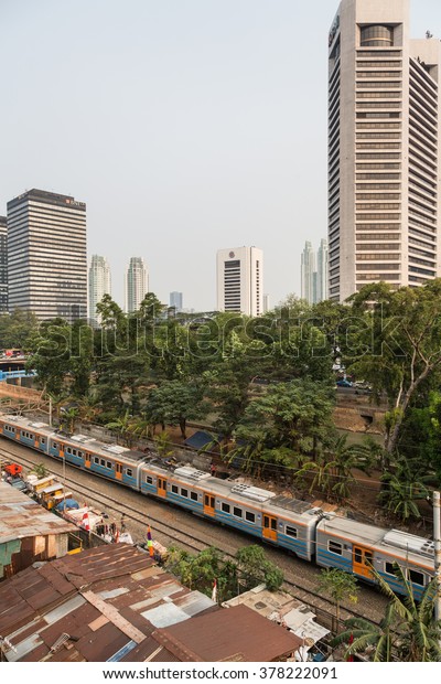 JAKARTA,\
INDONESIA - AUGUST 21 2015: A commuter train goes through a shanty\
town right next to the business district of Jakarta, where poverty\
contrasts with modern office in the\
background.