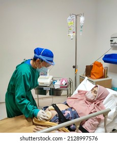 Jakarta, Indonesia - Jan 2022: Patient Laying On Bed Receiving Medical Treatment From Nurse With Green Uniform In Intensive Care Unit Room At Hospital.