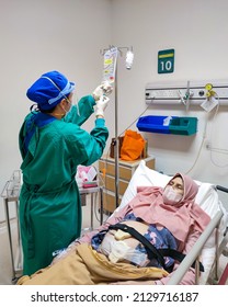 Jakarta, Indonesia - Jan 2022: Patient Laying On Bed Receiving Medical Treatment From Nurse With Green Uniform In Intensive Care Unit Room At Hospital.