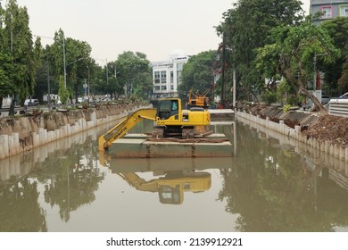 Jakarta, Indonesia - March 26 2022 : Yellow Excavator On A Floating Platform In A River Digging Cumulative Dirt That Shallowing The River, A Flood Management Project