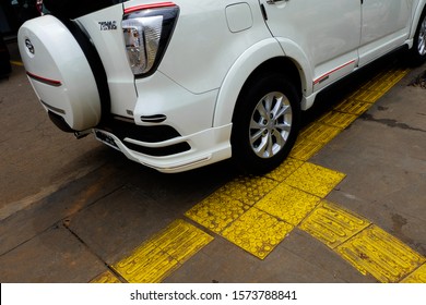 Jakarta, Indonesia - November 23 2019: White Car Parking on the Yellow Sidewalk Bump or Known as Tactile Paving or Detectible Warning Pavers in Jakarta. Facilities for Disabled and Disabilities.