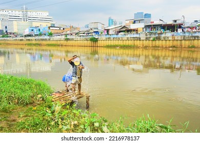 Jakarta, Indonesia - October 11, 2022: A Boy Is Cleaning His Clothes That Are Dirty From Mud With River Water In The Afternoon On The Bank Of The West Canal, Jakarta.