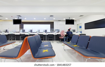 JAKARTA - Indonesia. October 21, 2020: Young Couple Wearing Face Mask While Sitting Near The Bank Counter With Empty Chair With Social Distancing Sign