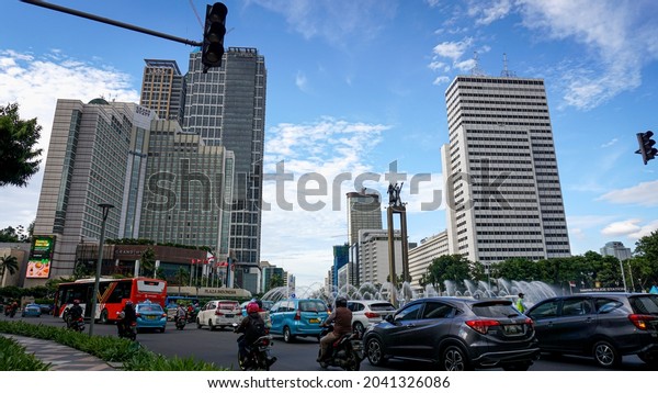 Jakarta, Indonesia: Traffic flow around the\
welcome monument \'Bundaran HI\', during the day in a clear blue sky\
(February 2020).