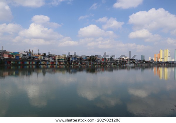 Jakarta, July 25, 2021. Tall buildings and rows of people's homes are painted in colors, under blue skies and white clouds, neatly arranged on the rim of lake sunter, the water like a mirror.