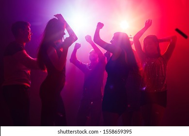 Jam session. A crowd of people in silhouette raises their hands on dancefloor on neon light background. Night life, club, music, dance, motion, youth. Purple-pink colors and moving girls and boys.
