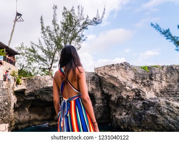 Jamaica - July 2018: Close up of brunette woman, in colourful outfit, looking out onto the cliffs and watching cliff jumping in Jamaica, Caribbean