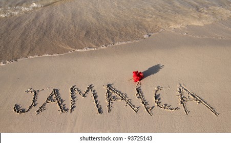 jamaica written on a beach with a red flower