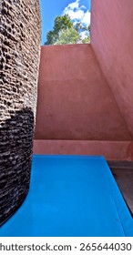James Turrell Within Without skyspace artwork at NGA Canberra Australia. A pyramid with soft red ochre interior walls with a stupa made of basalt highlighted by turquoise water. On a sunny day.