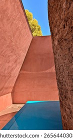 James Turrell Within Without skyspace artwork at NGA Canberra Australia. A pyramid with soft red ochre interior walls with a stupa made of basalt highlighted by turquoise water. On a sunny day.