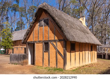 Jamestowne, VA, USA - April 1, 2013: Historic site. 1 replica house built on side. Brown-orange clay and dark reet and straw roof. Trees with few green leaves as backdrop. 