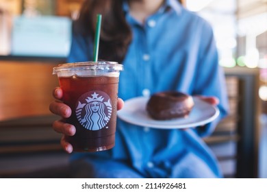 Jan 25th 2022 : Closeup of a woman holding and serving iced coffee and donut at Starbucks coffee shop , Chiang mai Thailand