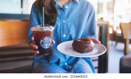 Jan 25th 2022 : Closeup of a woman holding and serving iced coffee and donut at Starbucks coffee shop, Chiang mai Thailand