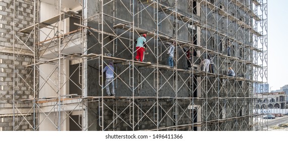 JANABIYA, BAHRAIN - OCTOBER 20, 2017: Asian Migrant Workers Plaster The Facade Of An Apartment Building On A Scaffolding Frame Of A Housing Development In The Middle East.