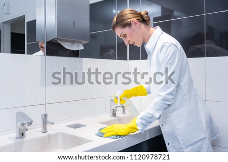 Janitor cleaning sink in public washroom with cloth 