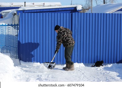 Janitor Cleans The Snow. The Man Shovels Away Snow In The Winter Outside. Shovel Being Pushed Through Snow. Man Clearing Street From Snow.  Man Cleans The Track About Of The Hoause, Sunny Winter Day.