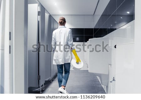 Janitor woman changing paper in public toilet or restroom 