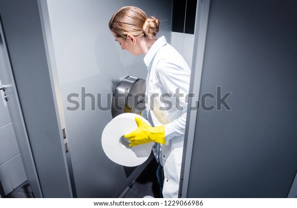 Janitor woman changing paper in public toilet or\
restroom 