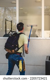 Janitor Worker Guy With Mask Cleaning Big Window Glass With Cleaning Tools In The Day