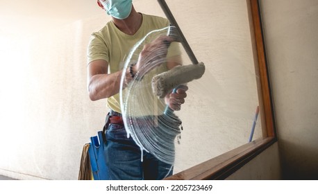 Janitor Worker Guy With Mask Cleaning Big Window Glass With Cleaning Tools In The Day