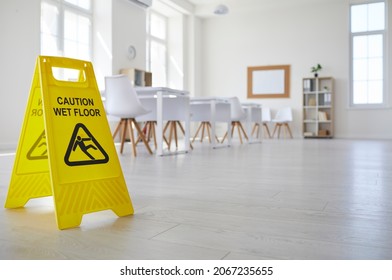 Janitorial Or Cleaning Service Plastic Sign With Figure That Slips And Falls And Words Caution Wet Floor Standing In Clean Empty Classroom With White Desks And Chairs At School, College Or University