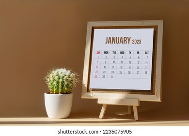 January 2023. Calendar for month on wooden stand next to green flower in pot, cactus. Sheet of white paper with days and weeks on desktop in rays of sunlight. Concept of New Year. - Shutterstock ID 2235075905