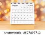 January 2025 desk calendar on wooden table with gold light bokeh background.