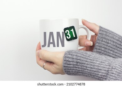 January 31st . Day 31 of month, Calendar date. Closeup of female hands in grey sweater holding cup of tea with month and calendar date on teabag label. Winter month, day of the year concept