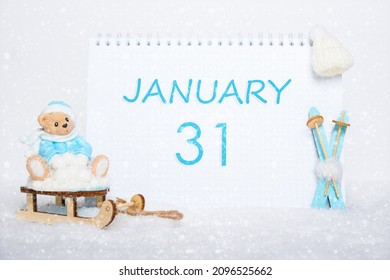 January 31st. Teddy bear sitting on a sled, blue skis and a calendar date on white snow. Day 31 of month.