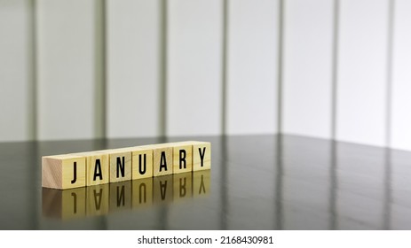 JANUARY Word On Wooden Cube On Black Gloss Wooden Table. Selected Focus