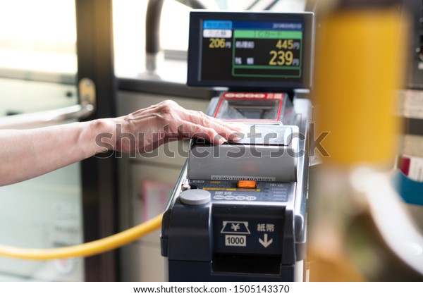 Japan, Tokyo - Sep 01 2019: Closeup of a\
eldery woman\'s hand waive a prepaid card on the contactless reader\
machine in a city bus. Public transportation, Japan\'s population\
ages, Senior discounts.