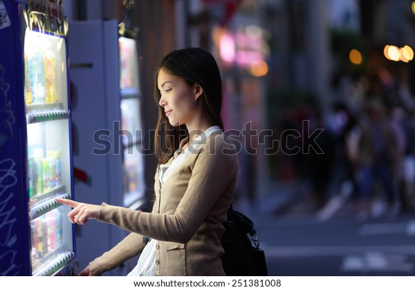 Japan vending machines - Tokyo woman buying\
drinks. Young student or female tourist choosing a snack or drink\
at vending machine at night in famous Harajuku district in Shibuya,\
Tokyo, Japan.