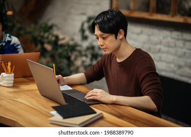 Japanese adult male drinking coffee and working via technology while sitting at the kitchen table