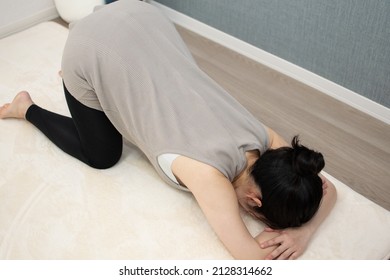 A Japanese Asian young beautiful pregnant woman lying on her stomach with relaxed clothes exercises regime to convert breech presentation on a white carpet from top angle