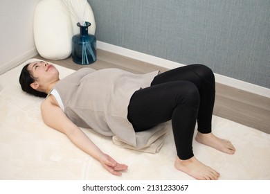 A Japanese Asian young beautiful pregnant woman lying on her back with relaxed clothes exercises regime to convert breech presentation on a white carpet from top angle
