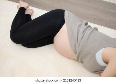 A Japanese Asian young beautiful pregnant woman lying on her side with relaxed clothes pulls up her clothes exercises regime to convert breech presentation on a white carpet with blue background from 