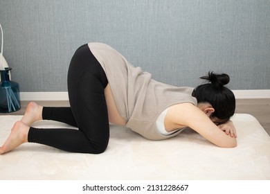A Japanese Asian young pregnant woman lying on her face with relaxed clothes pulls up her clothes, and exercises regime to convert breech presentation on a white carpet with blue back