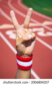 Japanese athlete with red and white wrist sweatband making a v-sign for victory with hand at a running track