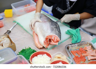 Japanese chef slicing raw fish for salmon sushi on a cutting board.