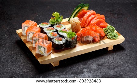 Japanese cuisine. Sushi set on a wooden plate over dark stone background.