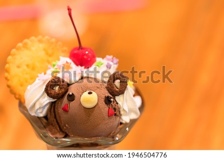 Japanese dessert in a stemware glass depicting ice cream shaped as a cute bear character in chocolate topped with sweet whipped cream, cookie and cherry fruit.