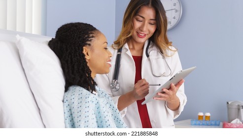 Japanese doctor talking to black patient in hospital bed with tablet computer