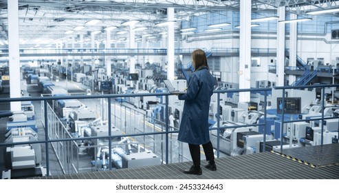 Japanese Factory Manager Working on Laptop at a Futuristic Industrial Manufacture with Autonomous AI Robots. Specialist Monitoring All the Data on a Computer, Checking Reports and Planning Research - Powered by Shutterstock