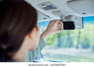Japanese female driver adjusting the rearview mirror of her car