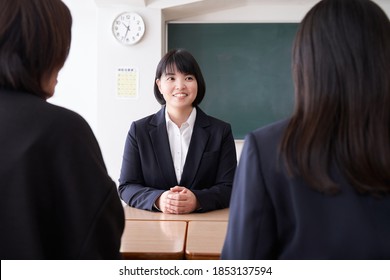 A Japanese Female Teacher Conducting A Three-way Interview In Her Classroom