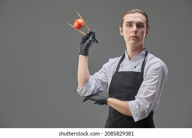 Japanese food. Portrait of a male chef holding a fresh ripe tomato with chopsticks on a gray background. Studio shot. - Powered by Shutterstock