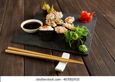Japanese food restaurant, sushi gunkan roll plate, platter set. Creative food. Set with chopsticks, ginger, soy, wasabi. Sushi at rustic wood background and black stone. POV, horizontal image Foto stock