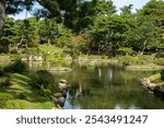 Japanese garden, the outdoor Shukkeien Garden in Hiroshima city with green pine trees at the Takueichi Pond at daytime during autumn season with sunshine in Japan.