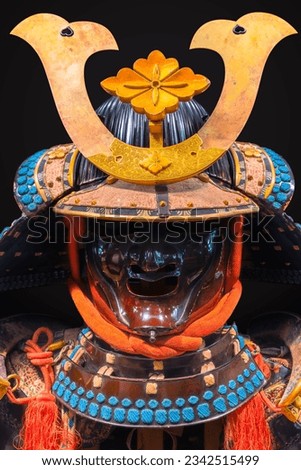 Japanese Kabuto helmet with a facial armor protecting the face adorned with a golden hanabishi crest part of a haramaki style armor laced with multi-colored threads.