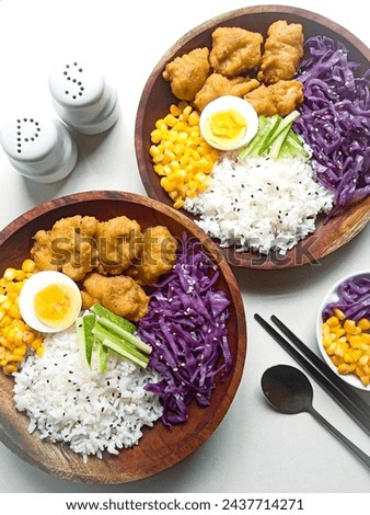 Japanese lunch idea. Steamed rice served with chicken tempura, boiled corn, boiled eggs, cucumbers, and purple cabbage. Two plates. Top view.